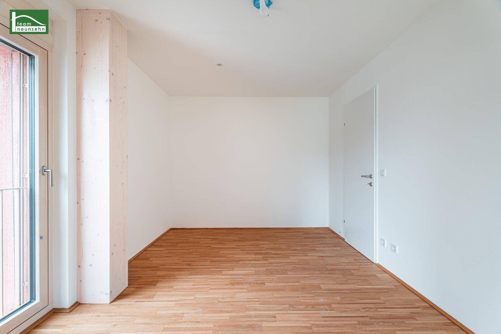Leeres Zimmer mit Holzboden und Fenstertür, bereit für individuelle Gestaltung.