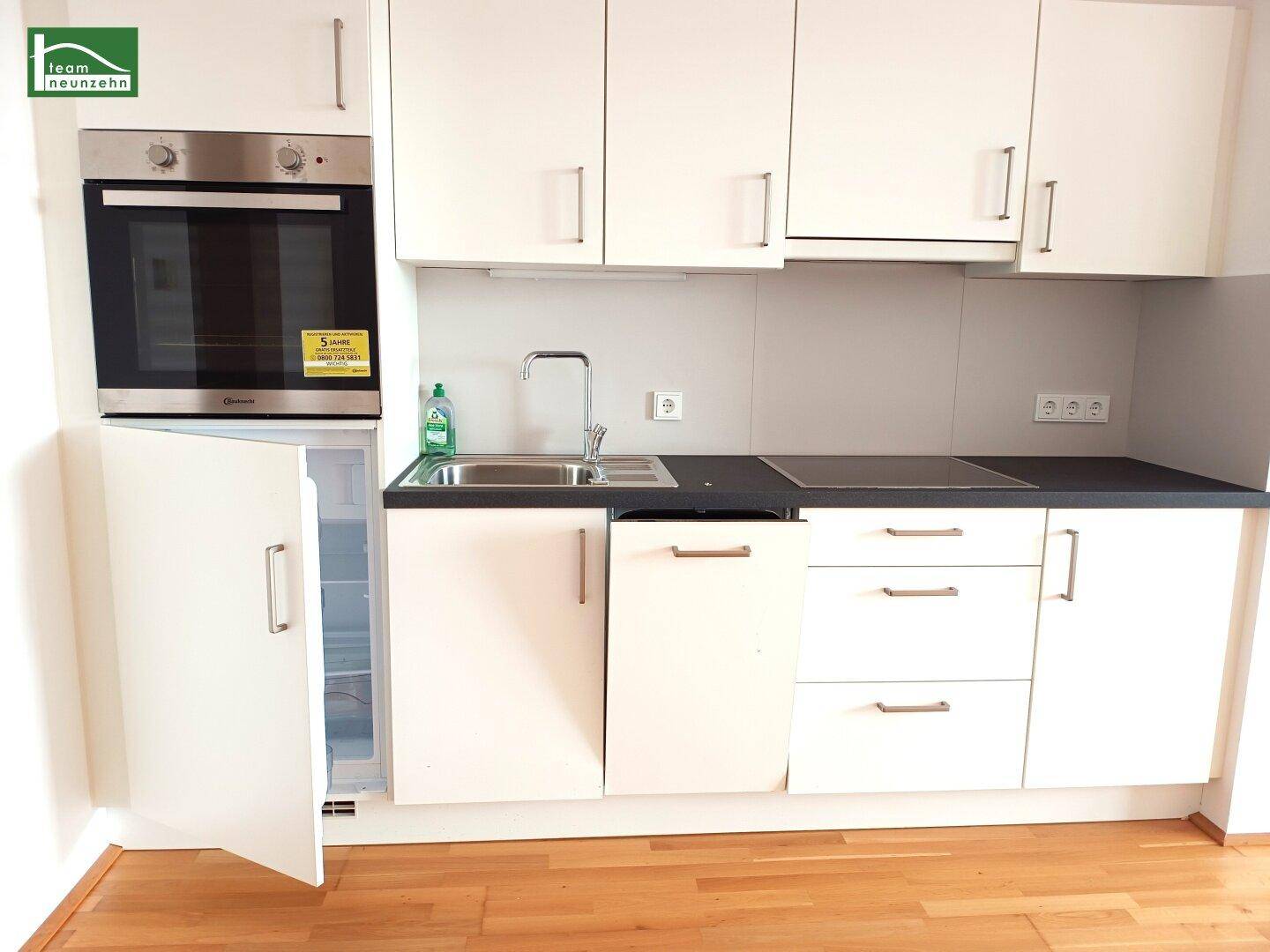 Kompakte Einbauküche mit weißen Schränken, Backofen und integriertem Kühlschrank.