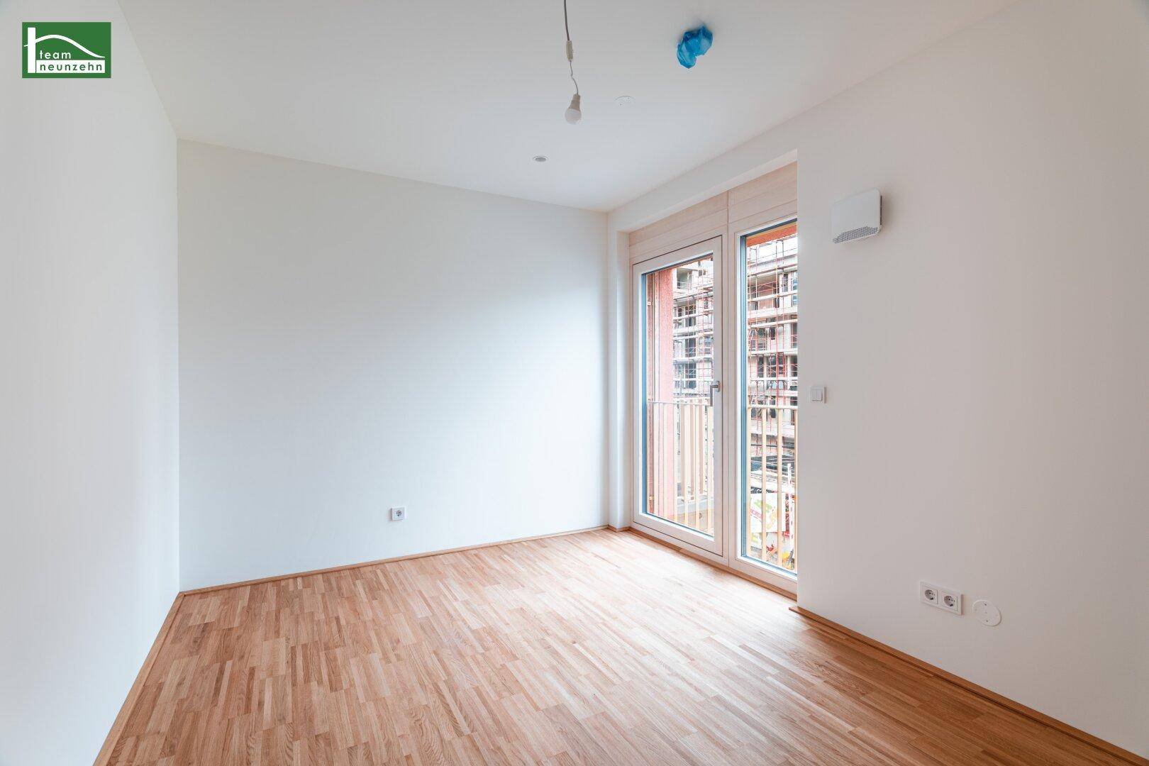 Helles Schlafzimmer mit Parkettboden und zwei französischen Balkonen, die den Raum erhellen.