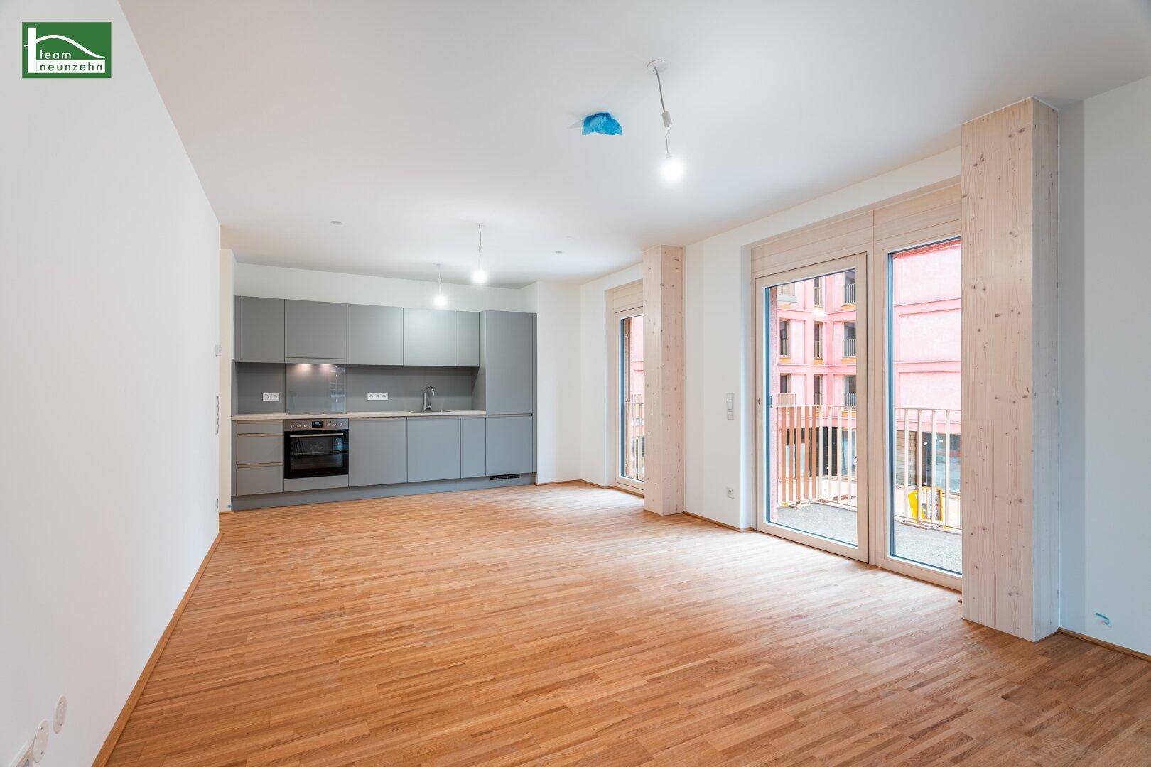 Offener Wohnbereich mit integrierter Küchenzeile, Parkettboden und Zugang zu einem französischen Balkon.