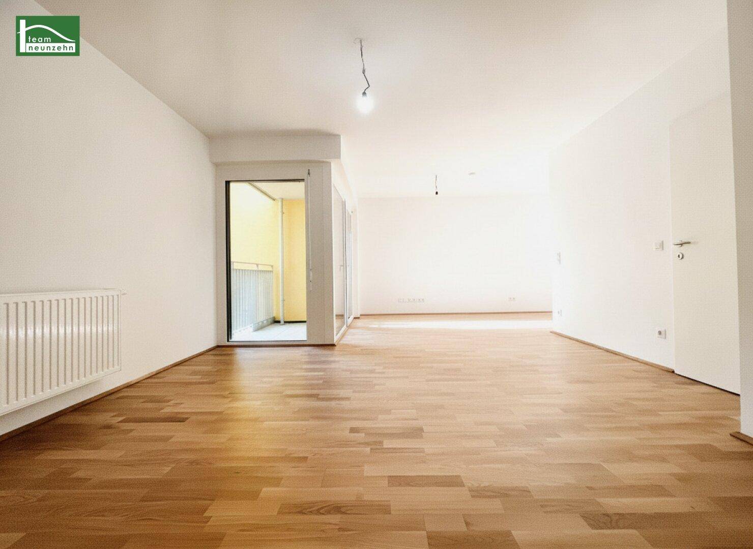 Geräumiges, leeres Zimmer mit hellem Parkettboden und Balkonzugang.
