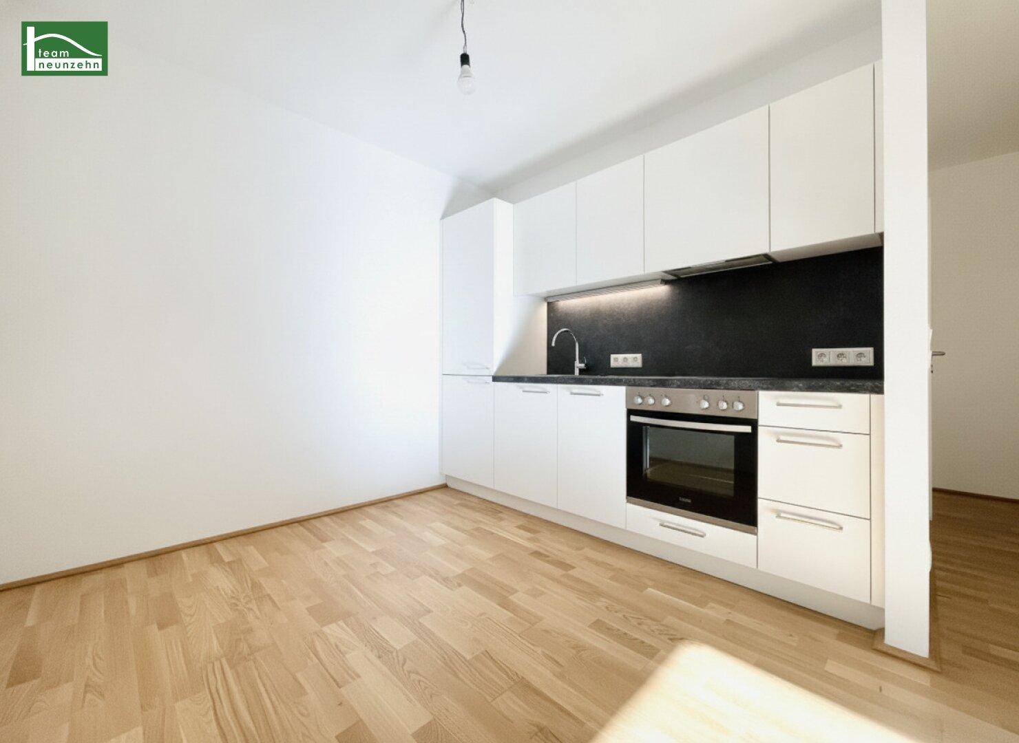 Moderne Einbauküche mit weißen Schränken, dunkler Arbeitsplatte und Parkettboden.