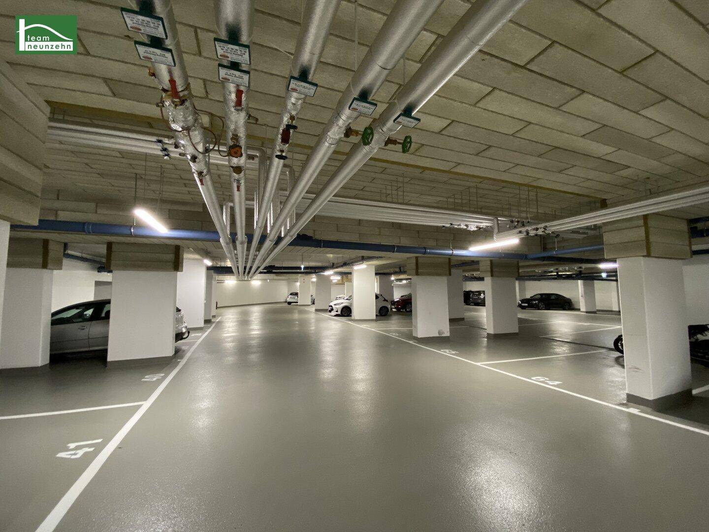 Tiefgarage mit markierten Stellplätzen, Betonpfeilern und sichtbaren Installationen.
