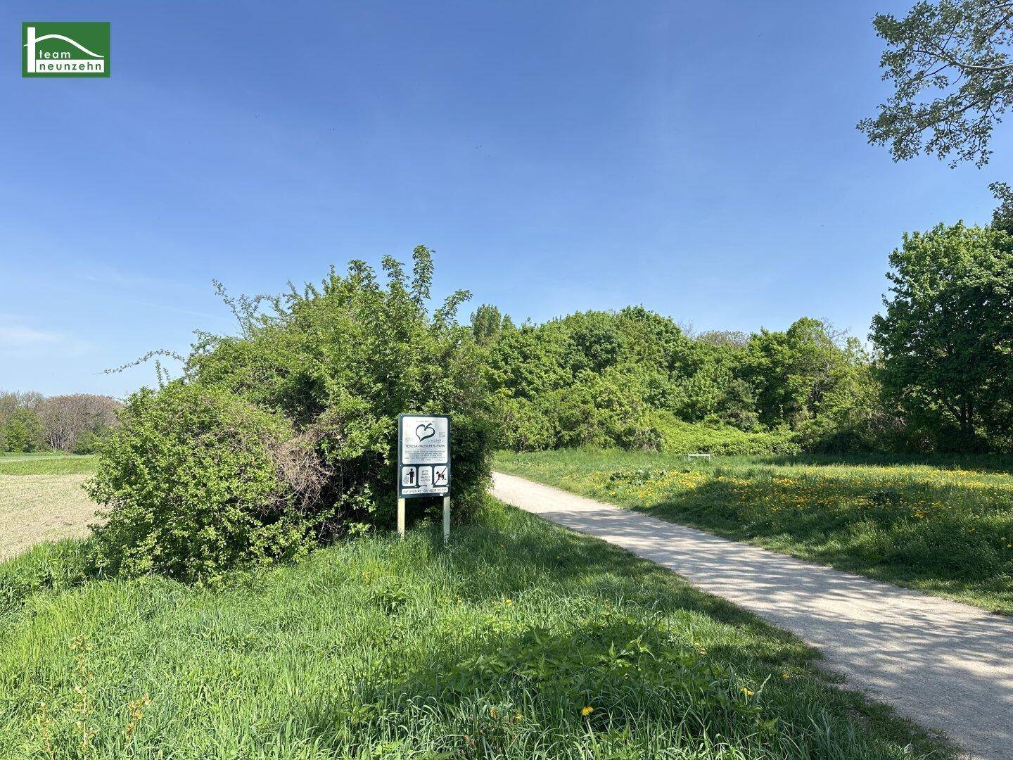 Naturlandschaft mit einem Spazierweg, üppigem Grün und einem Hinweisschild.