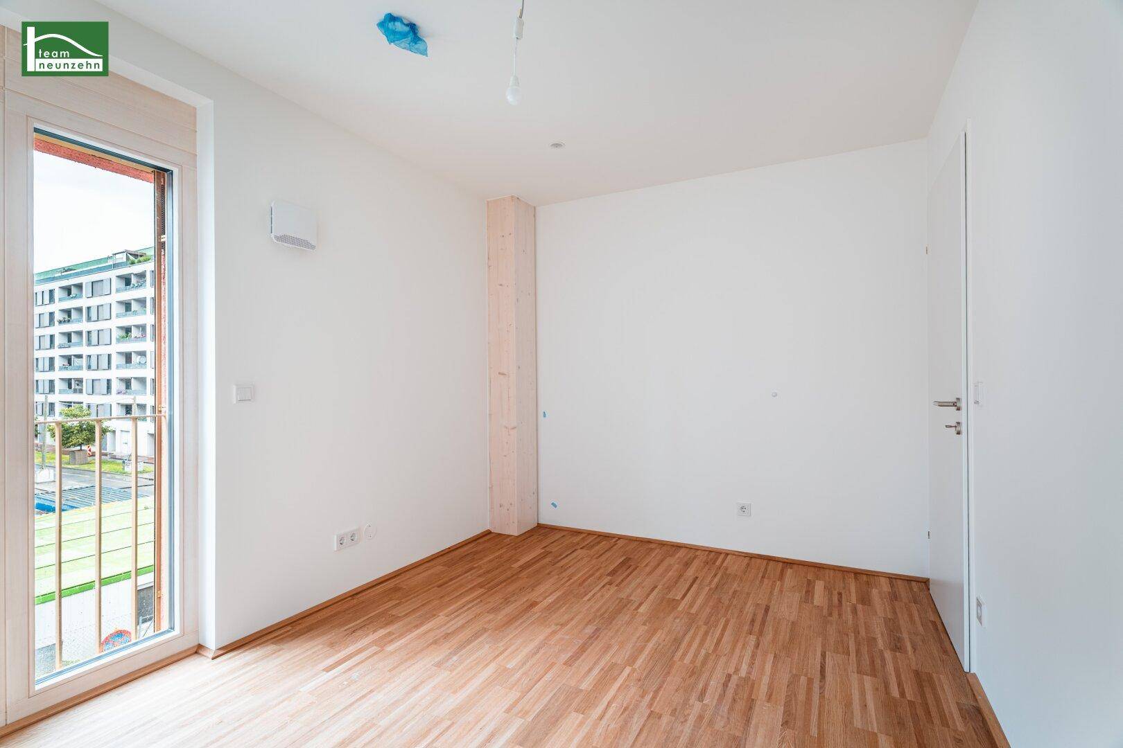Helles Zimmer mit Holzboden und Fenster mit Blick nach draußen.