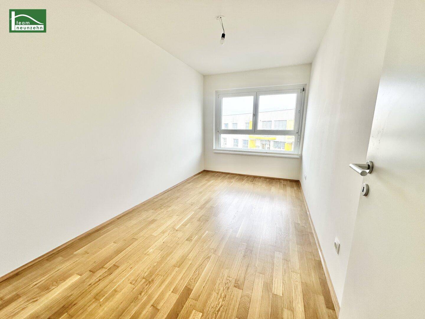Helles Schlafzimmer mit Holzparkettboden und großem Fenster mit Blick nach draußen.