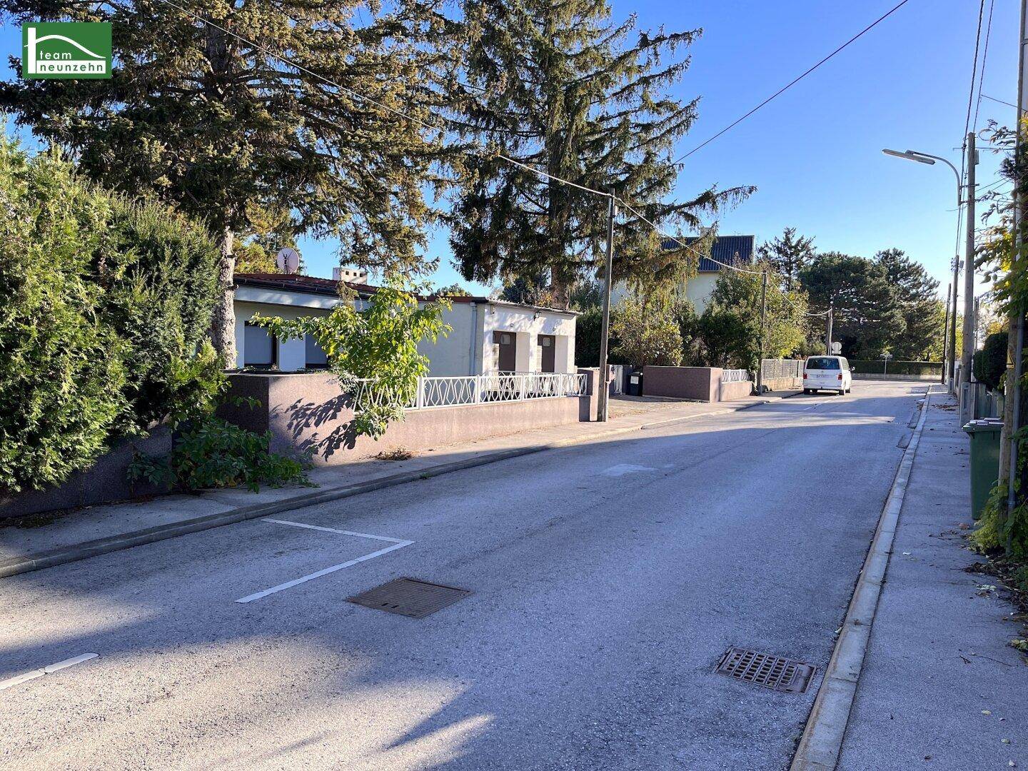 Blick von der Straße auf ein Einfamilienhaus mit Garten, Bäumen und einem Stellplatz.