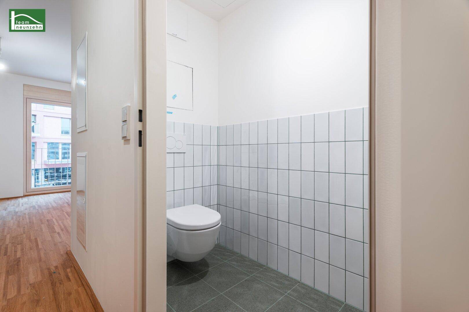 Separate Toilette mit wandhängendem WC und halbhoch gefliesten Wänden.