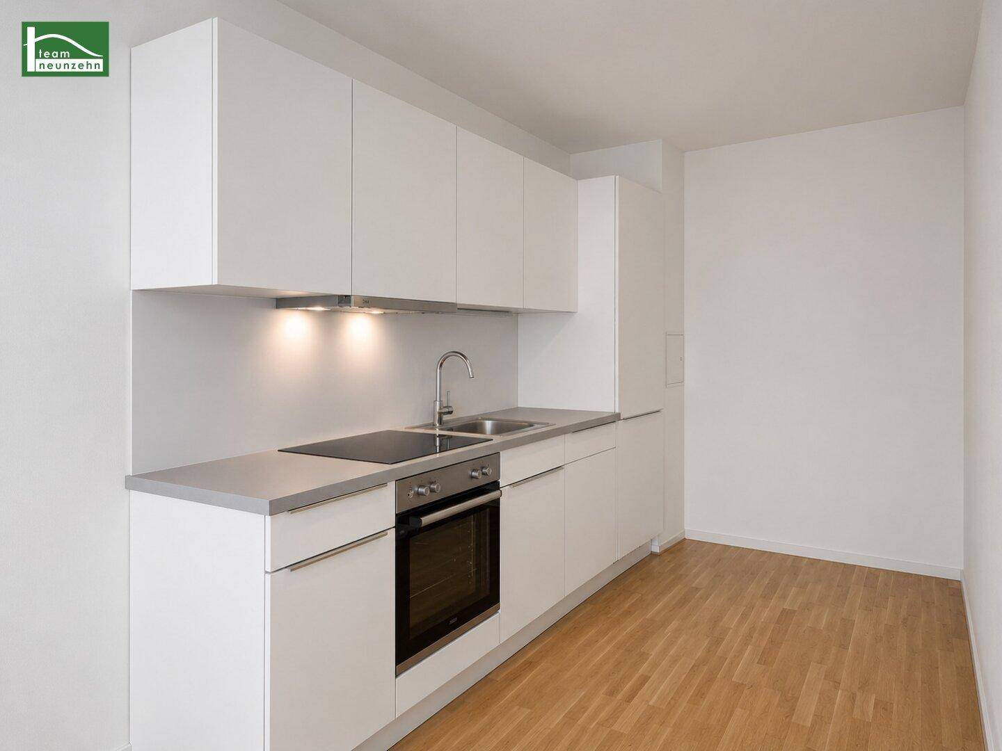 Moderne Einbauküche mit weißen Schränken, integrierten Geräten und Holzparkettboden.