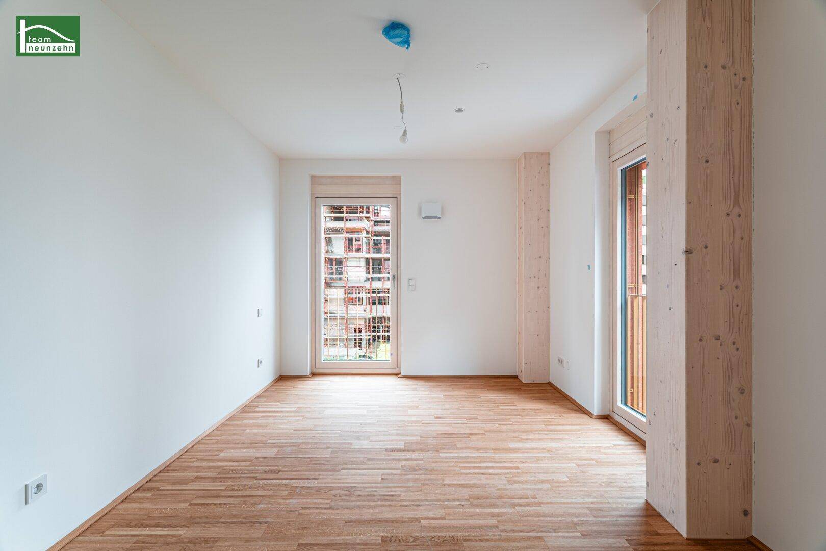 Geräumiger, unmöblierter Raum mit hellem Holzboden und zwei großen Fenstertüren.