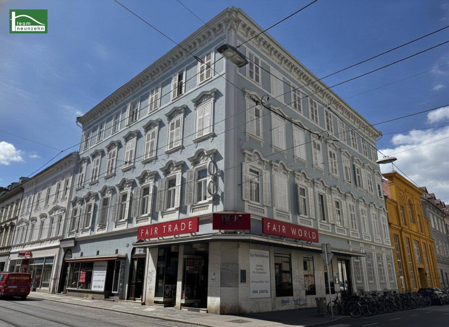 Historisches Gebäude mit klassischer Fassade und Geschäften im Erdgeschoss unter blauem Himmel.