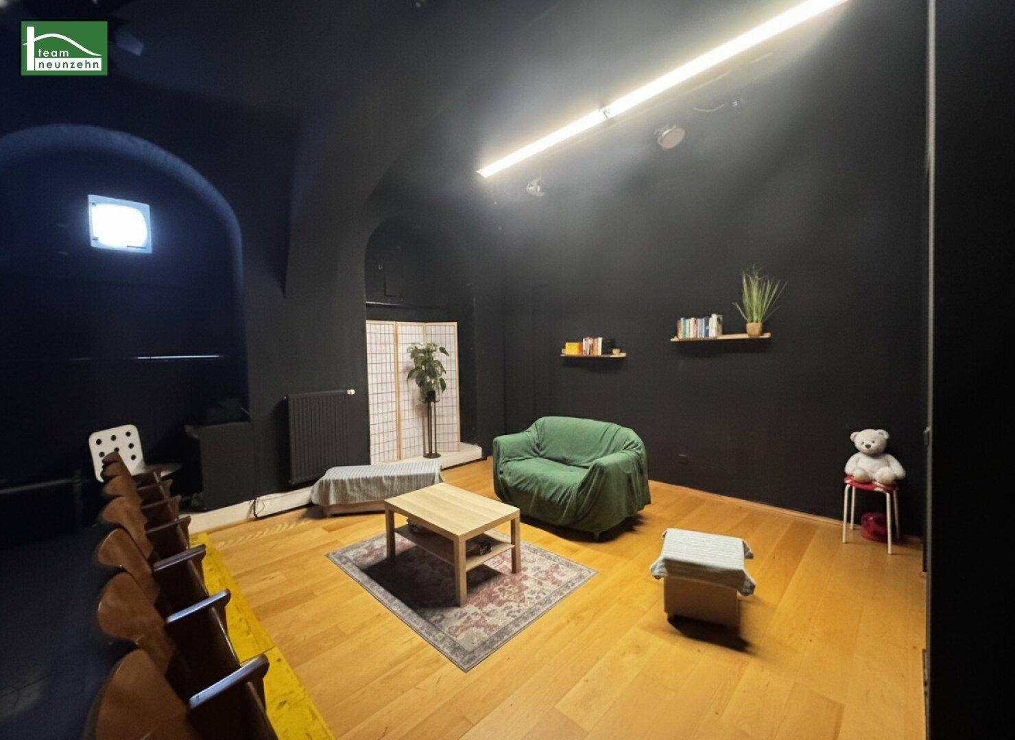 Vielseitiger Raum mit dunklen Wänden, Holzboden und einer kleinen Sitzecke mit Sofa.