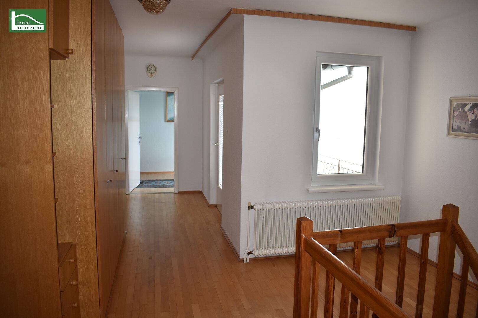 Heller Flur im Obergeschoss mit Holzschränken, Parkettboden und Treppengeländer.
