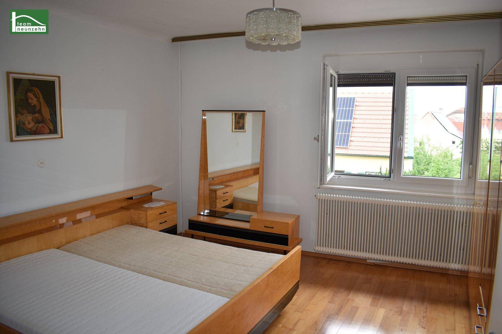 Schlafzimmer mit Doppelbett, Holzmöbeln und Fenster mit Blick auf die Umgebung und Solaranlage.