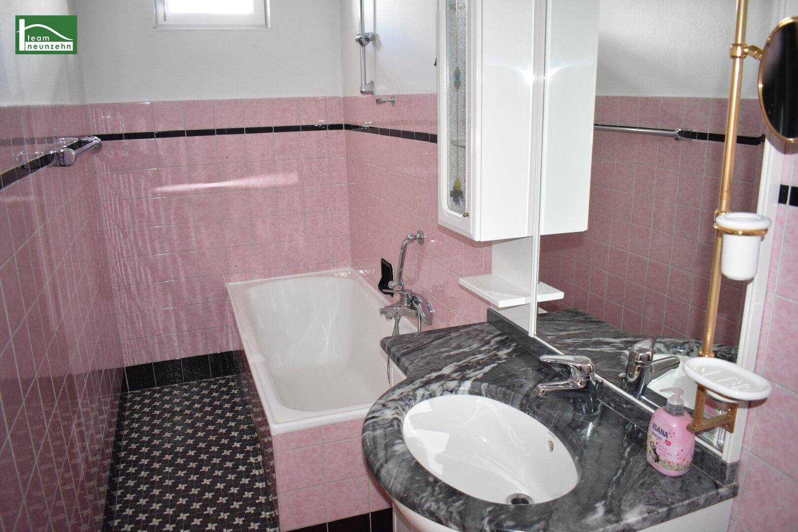 Badezimmer im 80er-Jahre-Stil mit rosa Fliesen, Badewanne und Marmorwaschtisch.