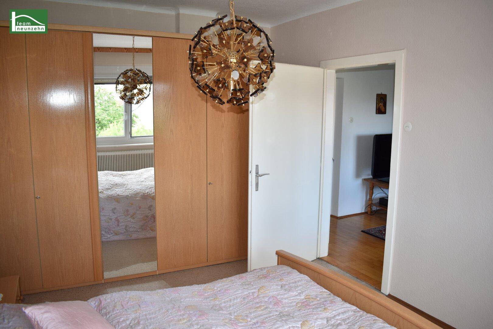 Schlafzimmer mit Doppelbett, Spiegelschrank und Zugang zu einem weiteren Raum.