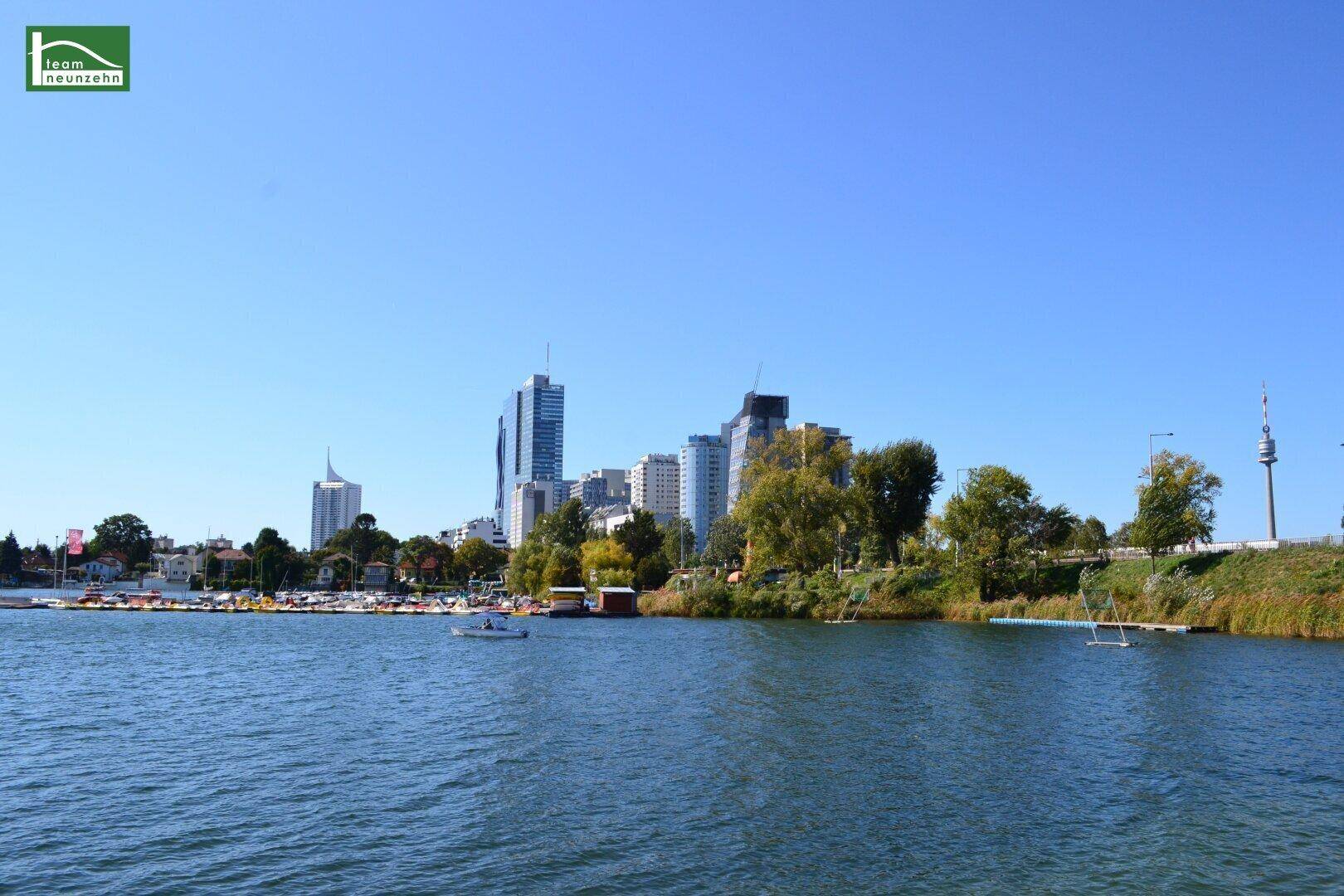 Panoramablick auf die moderne Stadtkulisse mit Hochhäusern, einem See und einem Yachthafen unter blauem Himmel.
