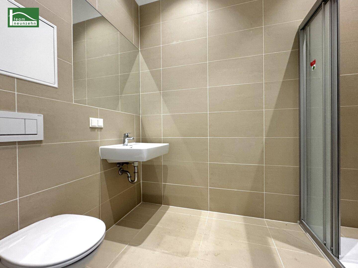 Modernes Badezimmer mit beigen Fliesen, wandhängendem WC, Waschbecken und Duschkabine.