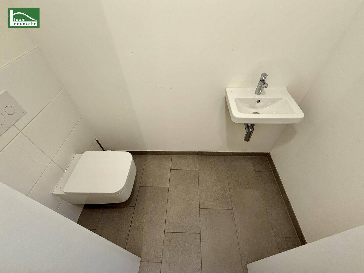 Separates Gäste-WC mit wandhängender Toilette, kleinem Waschbecken und Fliesenboden.