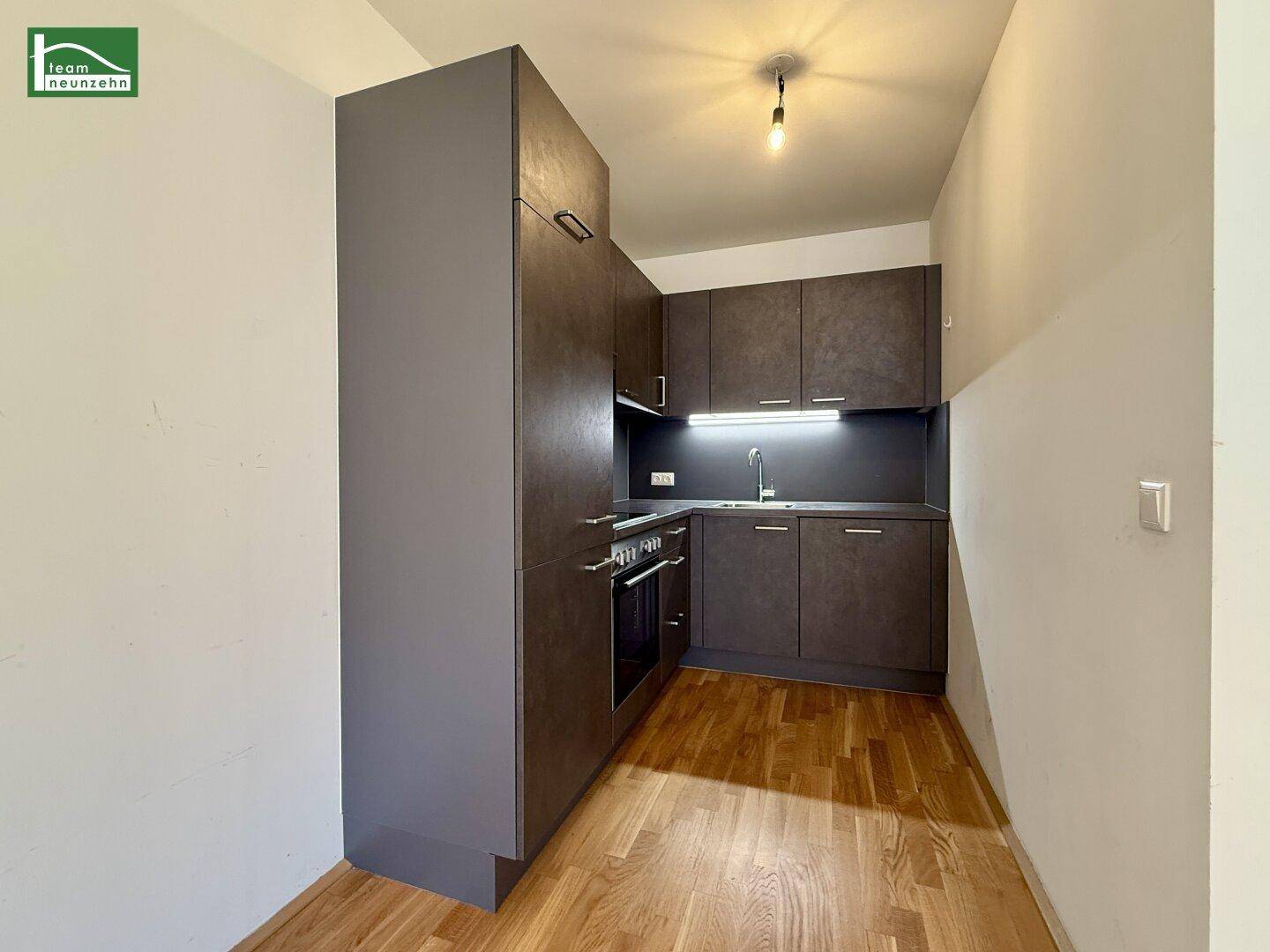 Moderne Einbauküche in dunklem Design mit integriertem Backofen und Holzboden.