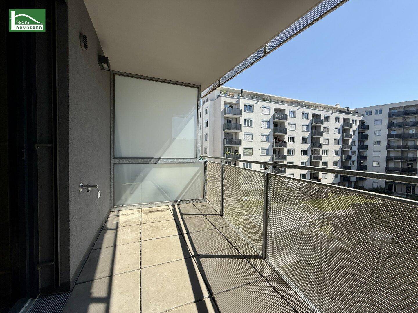 Heller Balkon mit Fliesenboden und Metallgeländer, bietet einen Blick auf die umliegenden Gebäude.