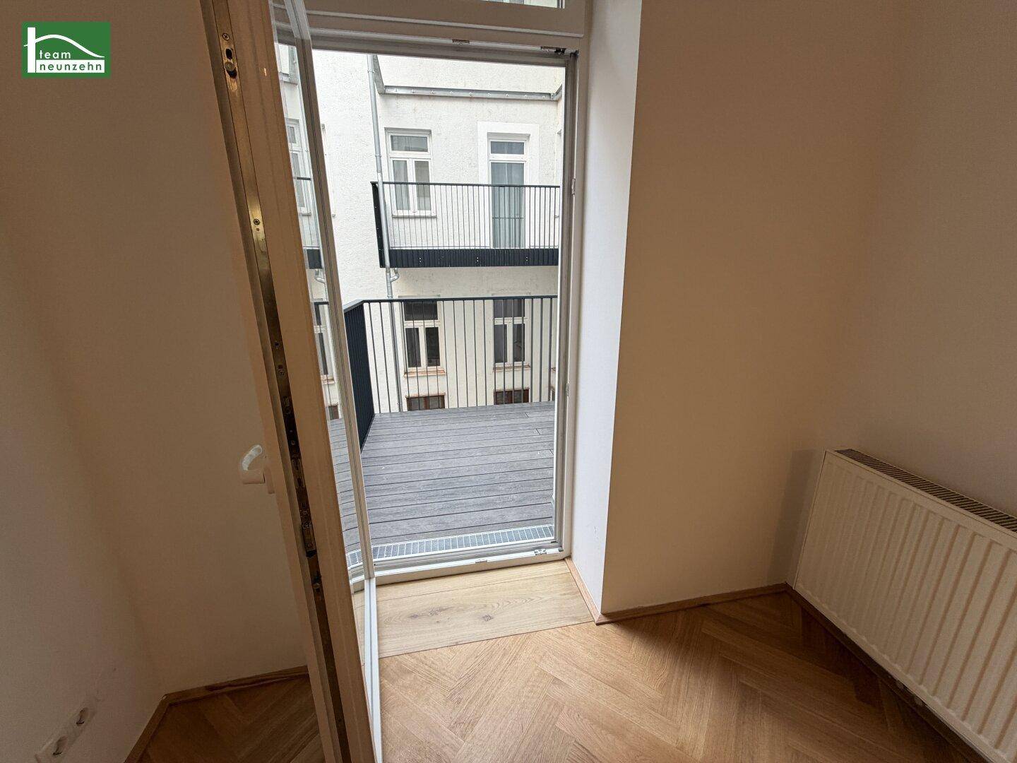 Heller Innenraum mit elegantem Fischgrätparkett und Zugang zu einem modernen Balkon mit Innenhofblick.