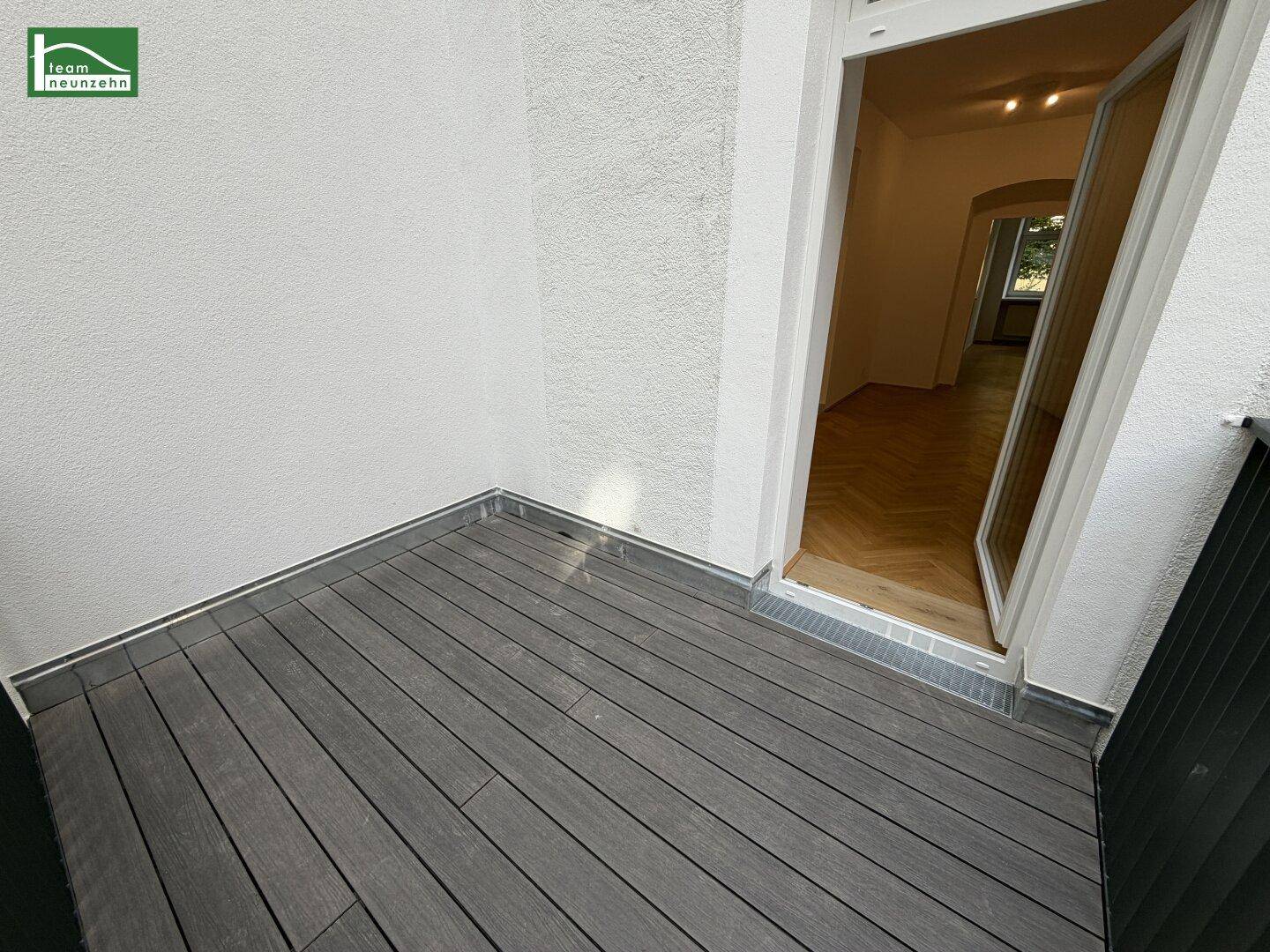 Heller Balkon mit modernem Bodenbelag und direktem Zugang zu einem Innenraum mit Fischgrätparkett.