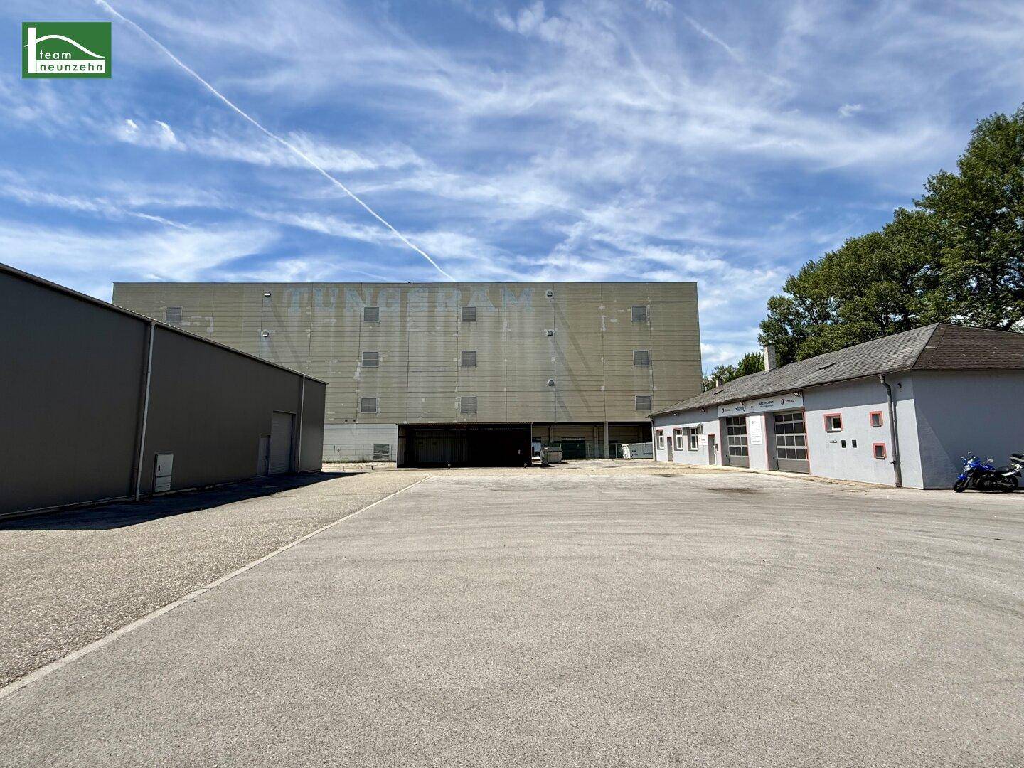 Weitläufiger Außenbereich mit mehreren Gewerbegebäuden und großem Parkplatz unter blauem Himmel.
