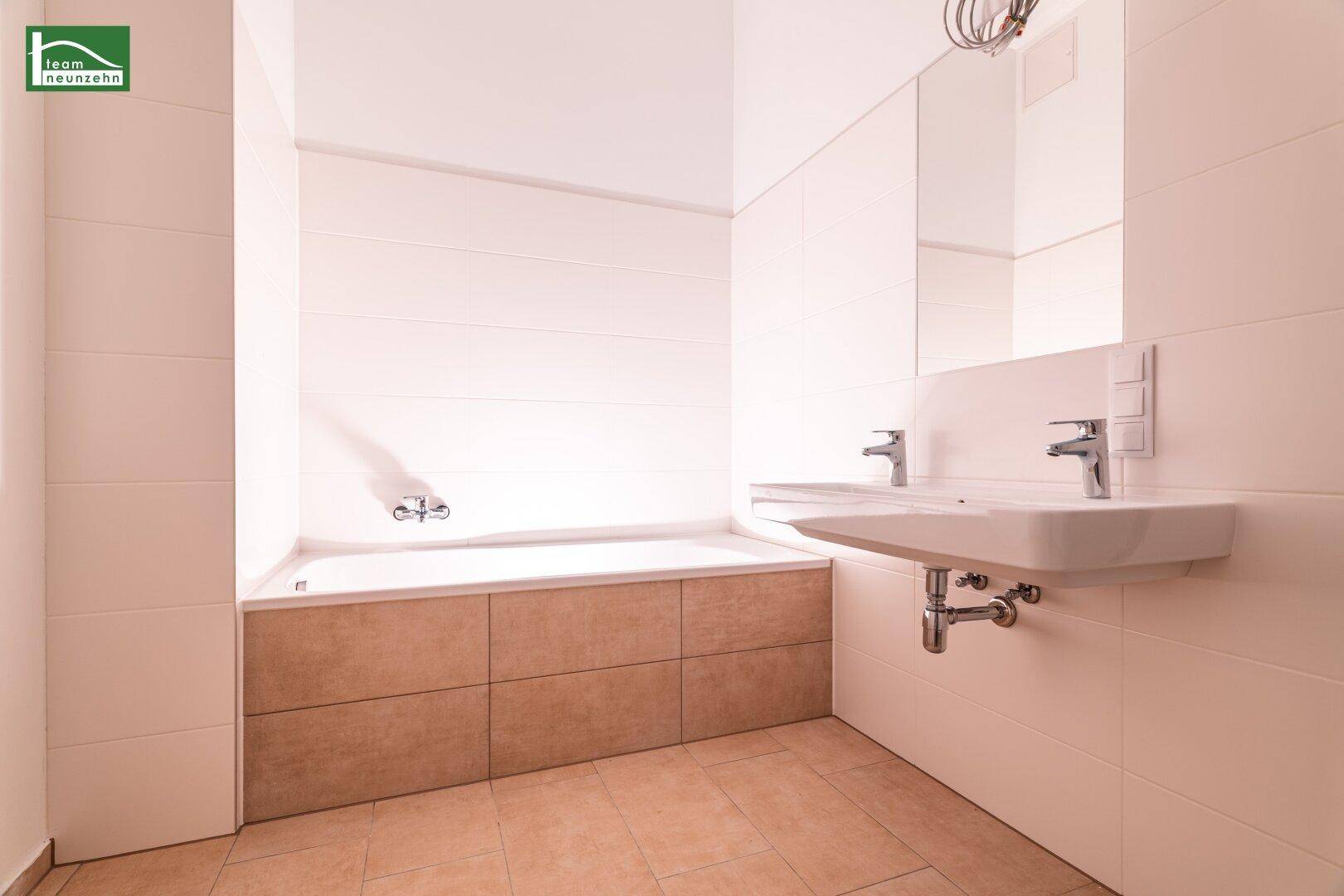 Modernes Badezimmer mit Badewanne, Doppelwaschbecken und hellen Fliesen an Wänden und Boden.
