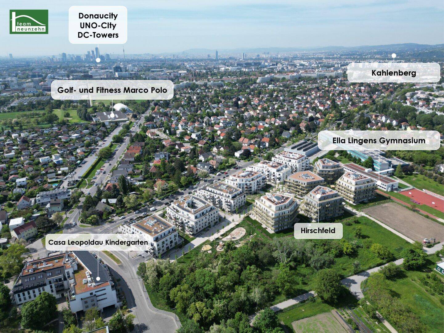 Luftaufnahme des Wohngebiets mit modernen Neubauten, umgeben von viel Grün und Blick auf die Stadt.