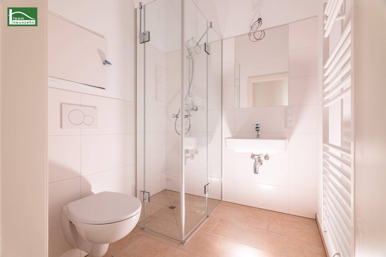 Funktionales Badezimmer mit weiß gefliesten Wänden, Duschkabine und Wand-WC.
