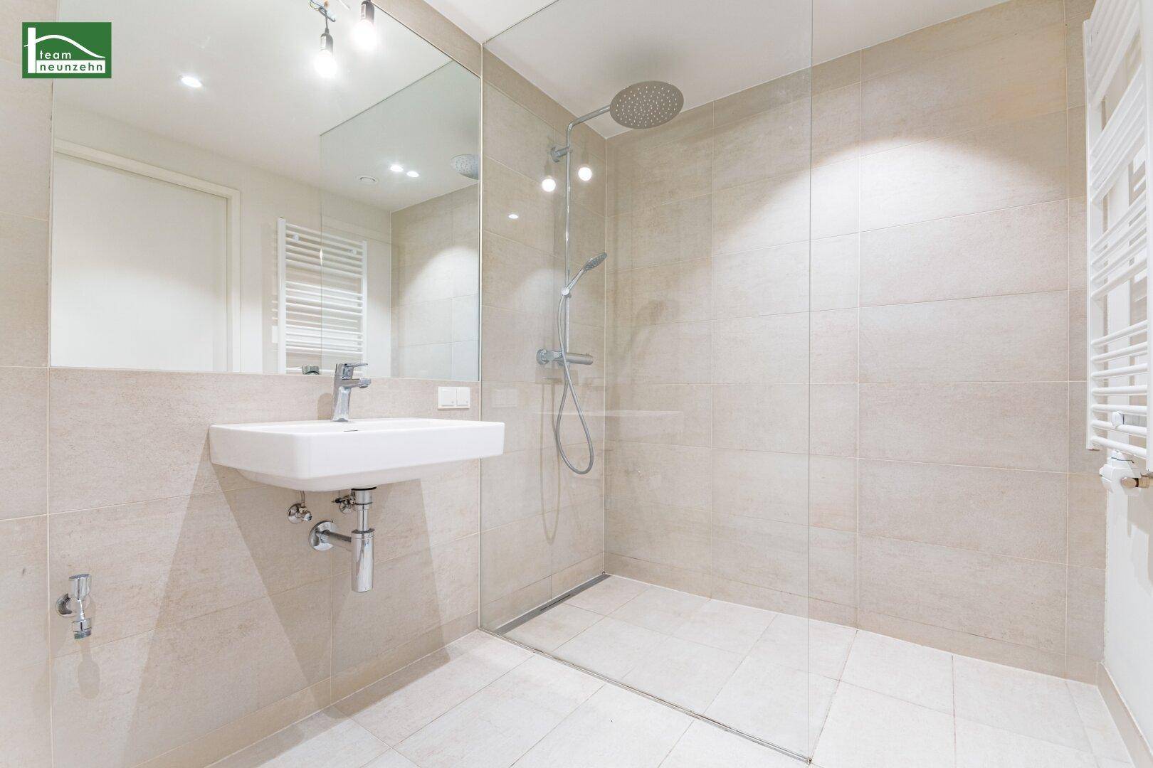 Modernes Badezimmer mit begehbarer Dusche, großem Spiegel und hellen Fliesen.
