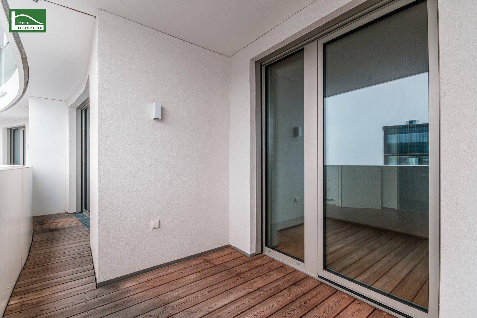 Heller Balkon mit Holzboden und großen Glasschiebetüren, ideal für entspannte Stunden im Freien.