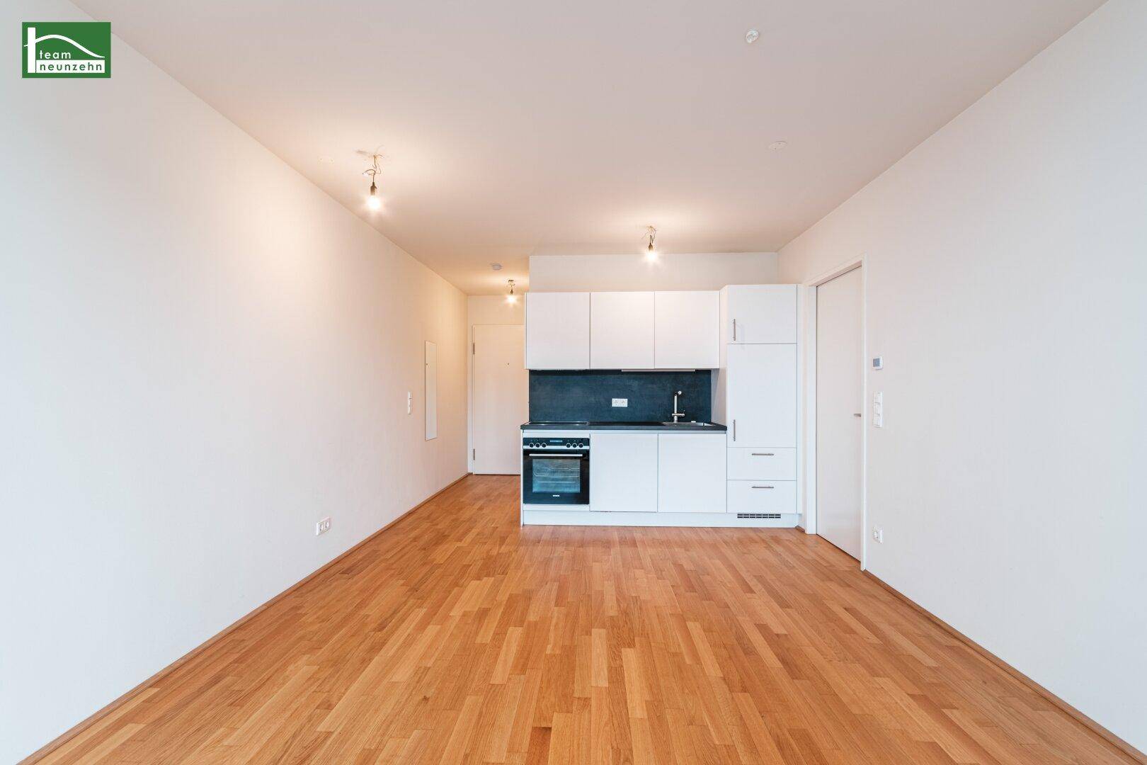 Moderne, offene Küche in einem hellen Raum mit Holzboden und weißen Wänden.