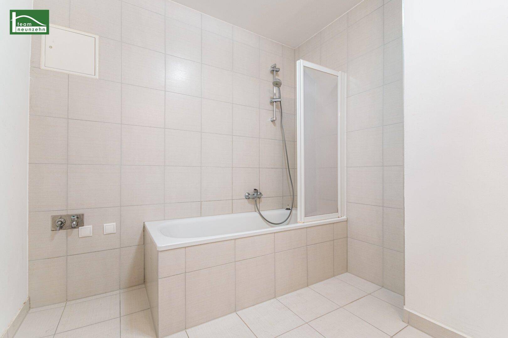 Badezimmer mit Badewanne, Duschabtrennung und hellen Fliesen an Wänden und Boden.