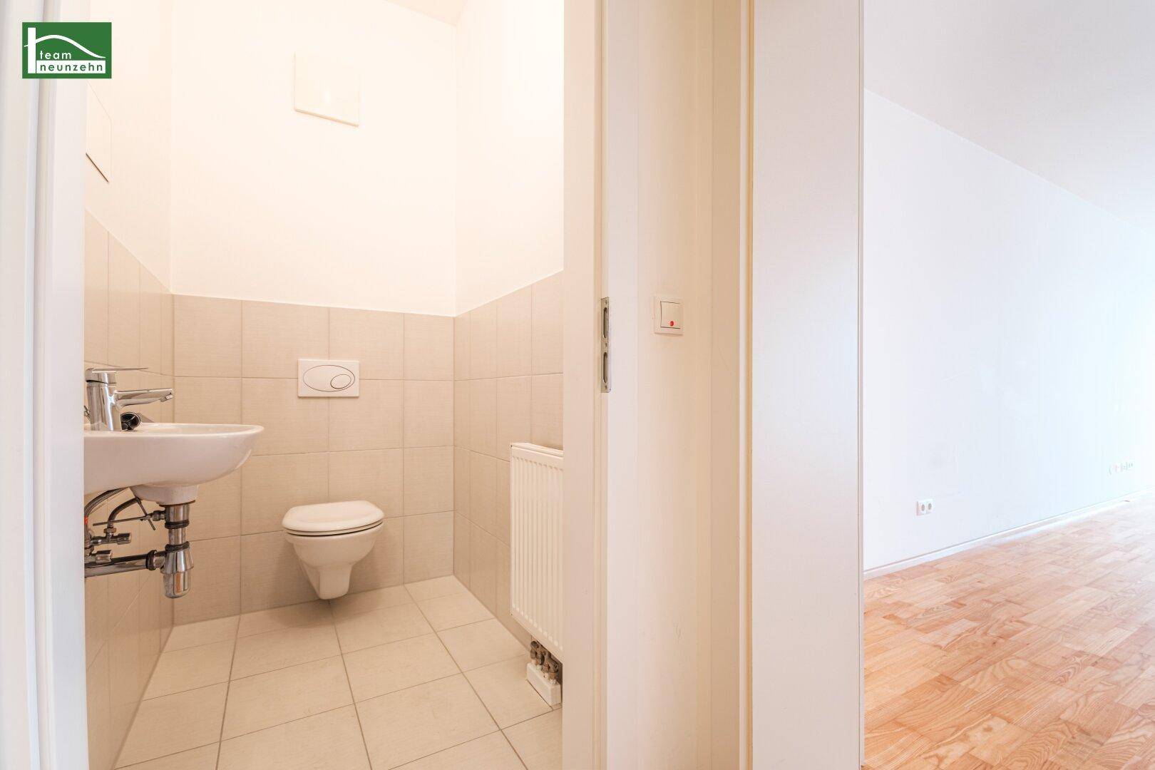 Separates Gäste-WC mit wandhängender Toilette, kleinem Waschbecken und hellen Fliesen.