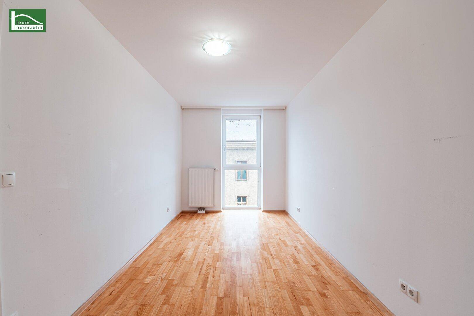 Helles, unmöbliertes Schlafzimmer mit Parkettboden und einem großen Fenster, ideal für Ruhe.