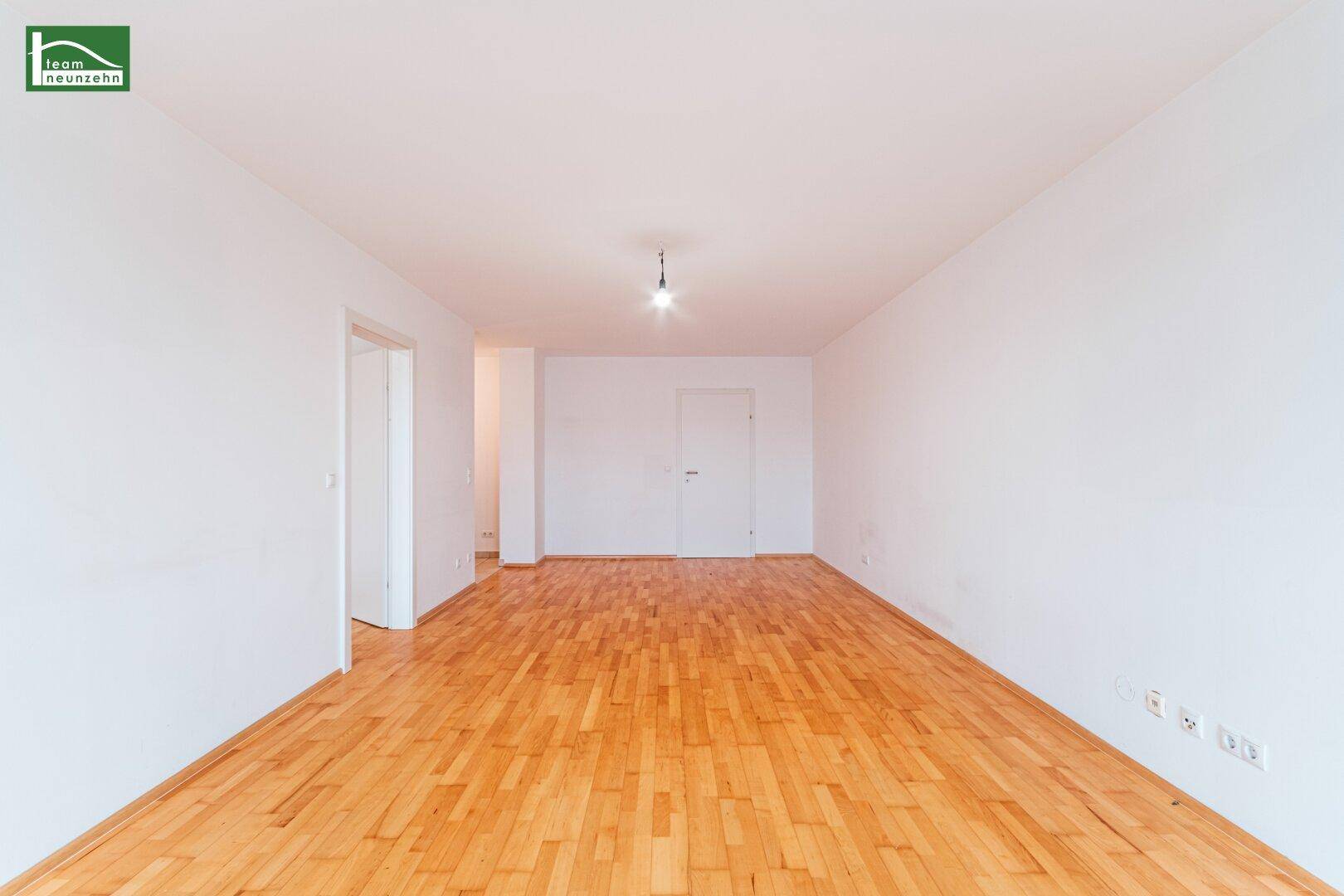Geräumiges, unmöbliertes Wohnzimmer mit hellem Parkettboden und weiß gestrichenen Wänden.