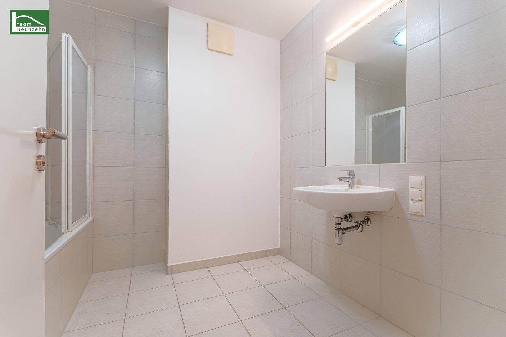 Modernes Badezimmer mit Waschbecken, großem Spiegel und hellgrauen Fliesen.