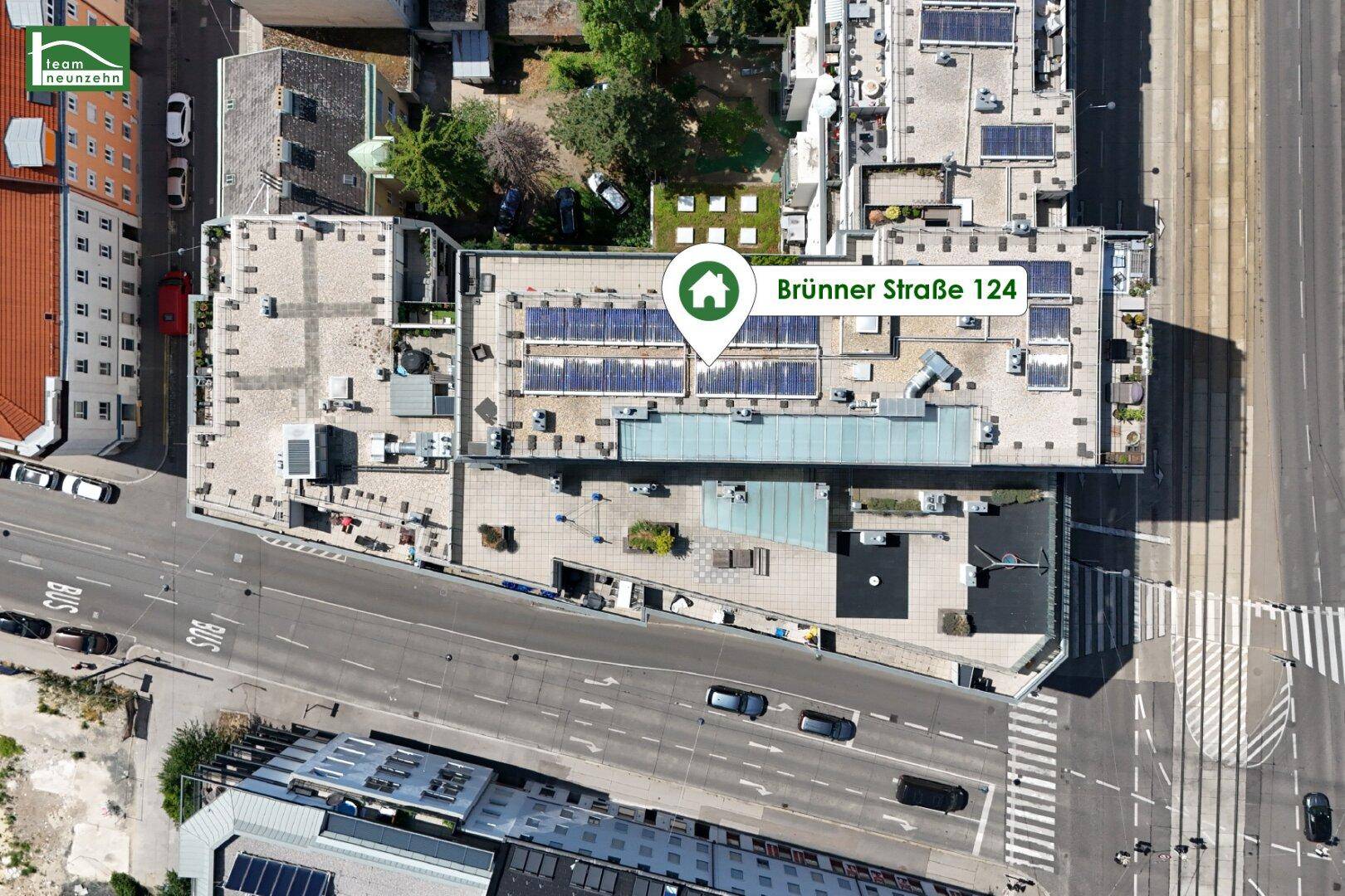 Vogelperspektive des Gebäudes mit Solaranlagen auf dem Dach und umliegenden Straßen.