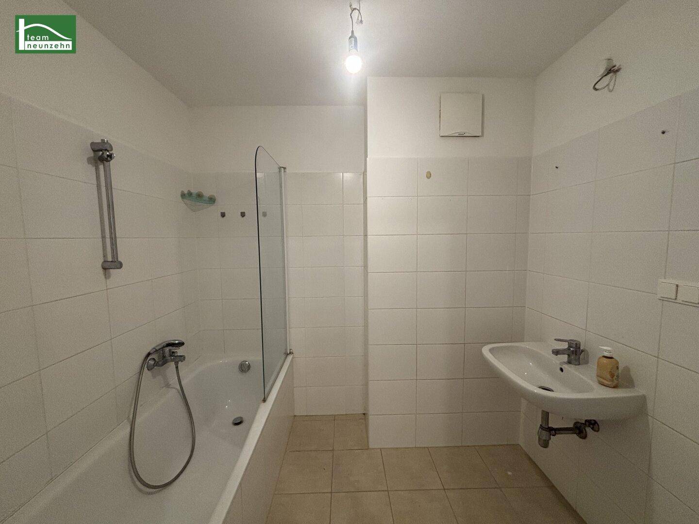 Funktionales Badezimmer mit Badewanne, Duschwand und Waschbecken, komplett gefliest.