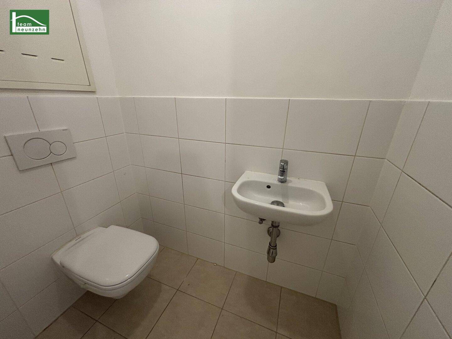 Gäste-WC mit wandhängender Toilette und kleinem Waschbecken, komplett gefliest.