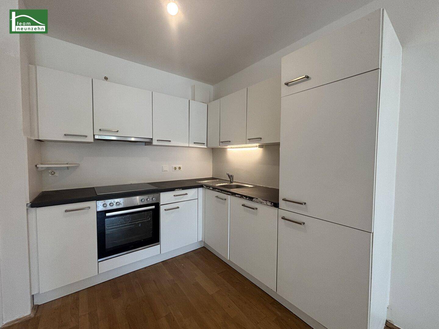 Moderne Einbauküche mit weißen Fronten, dunkler Arbeitsplatte und integrierten Geräten.