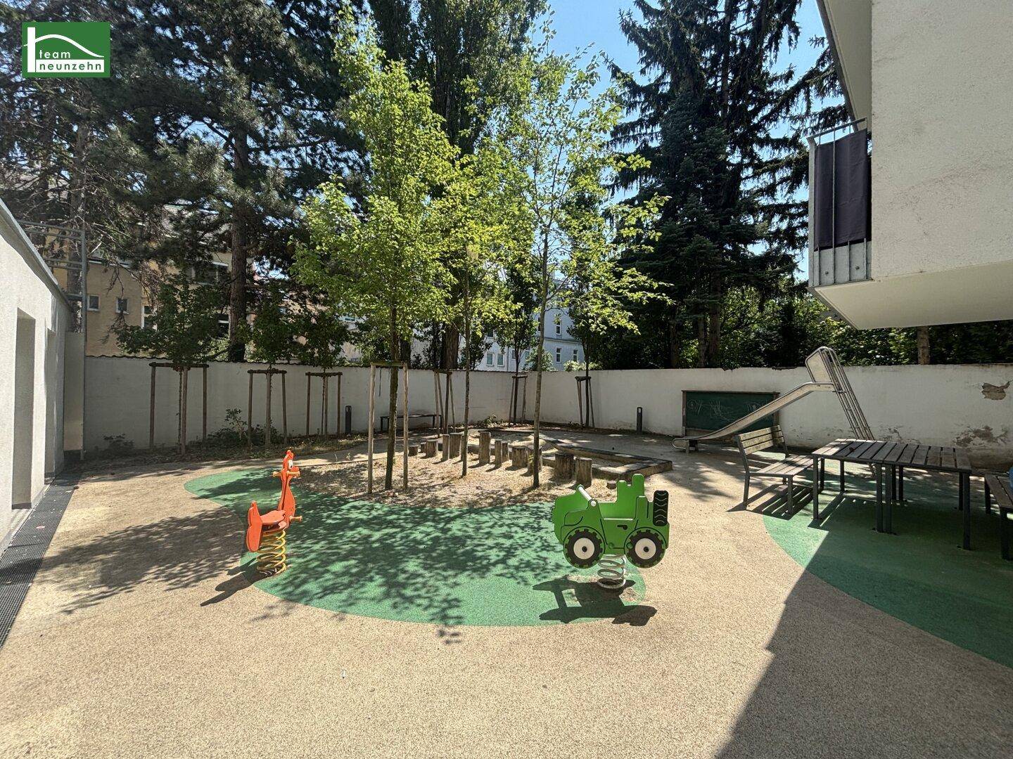 Gemeinschaftlicher Spielplatz im Freien mit verschiedenen Spielgeräten und Bäumen.