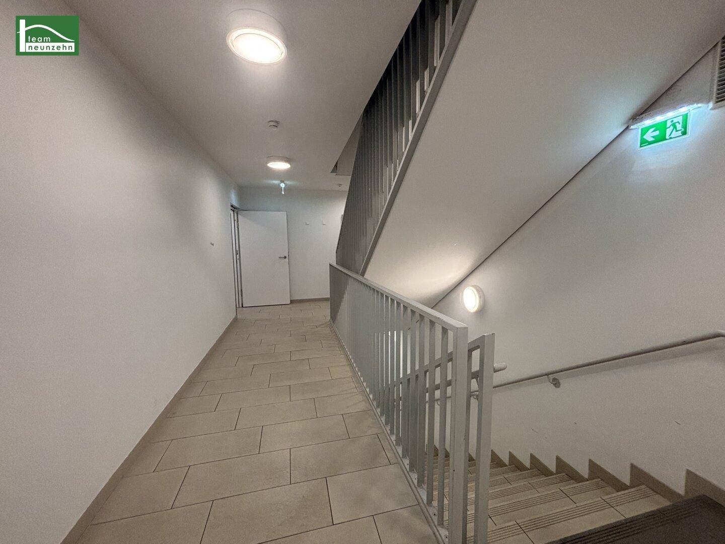 Treppenhaus mit gefliestem Boden und modernem Geländer, gut beleuchtet.