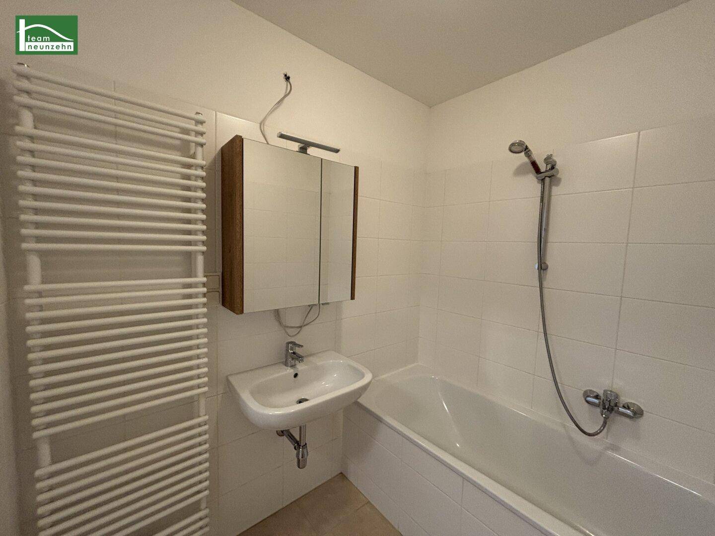 Modernes Badezimmer mit weißen Fliesen, Badewanne mit Duschfunktion und beheiztem Handtuchhalter.