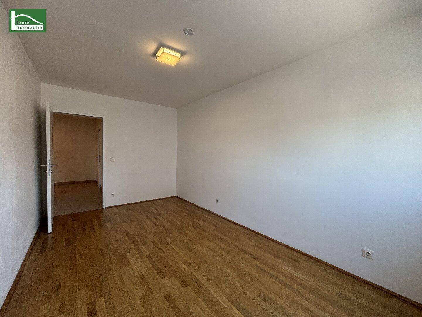 Leeres Zimmer mit Parkettboden und einer Tür, die zu einem weiteren Raum führt, in gutem Zustand.