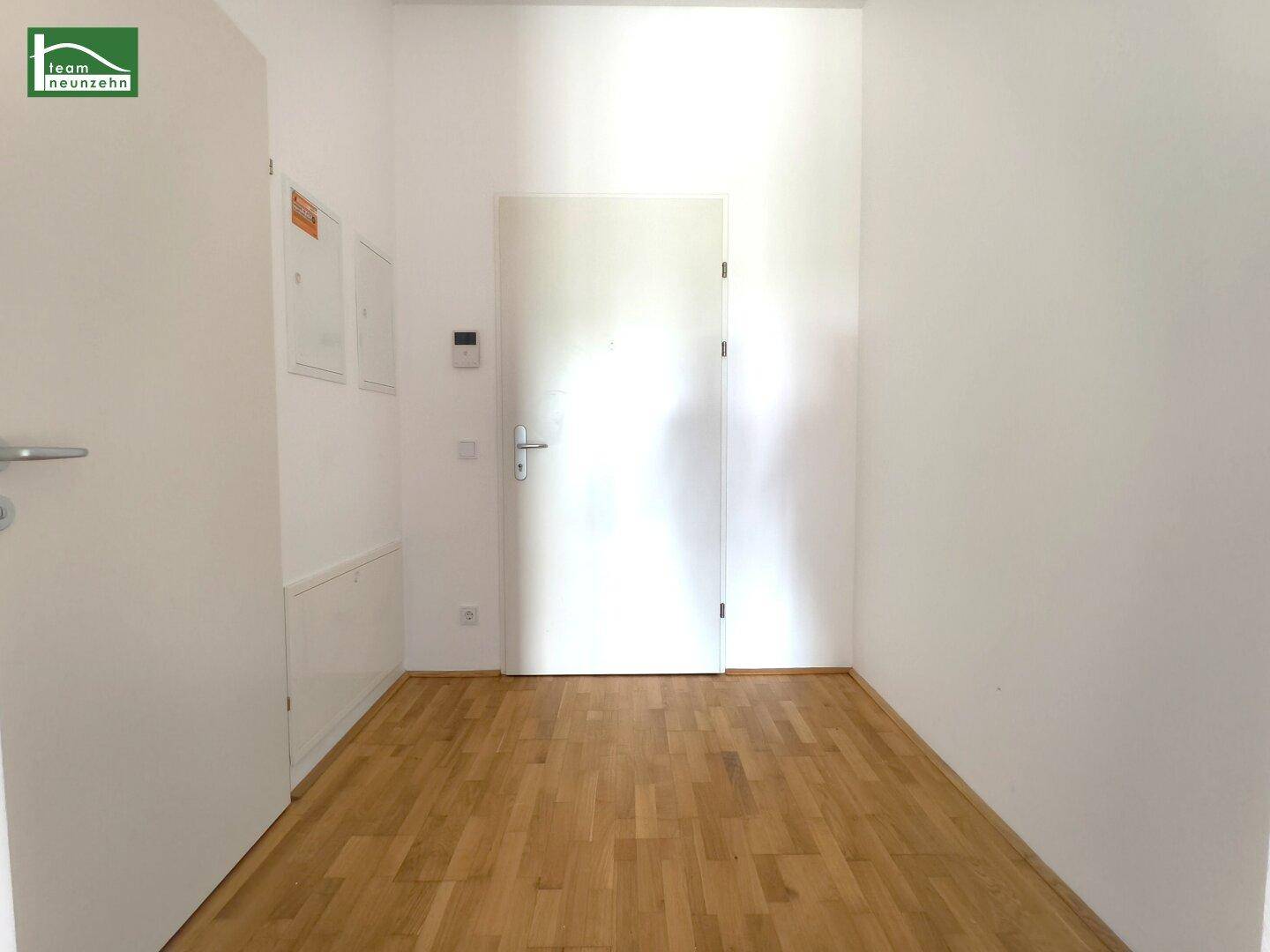 Heller Eingangsbereich mit Eichenparkettboden und weißer Wohnungstür.