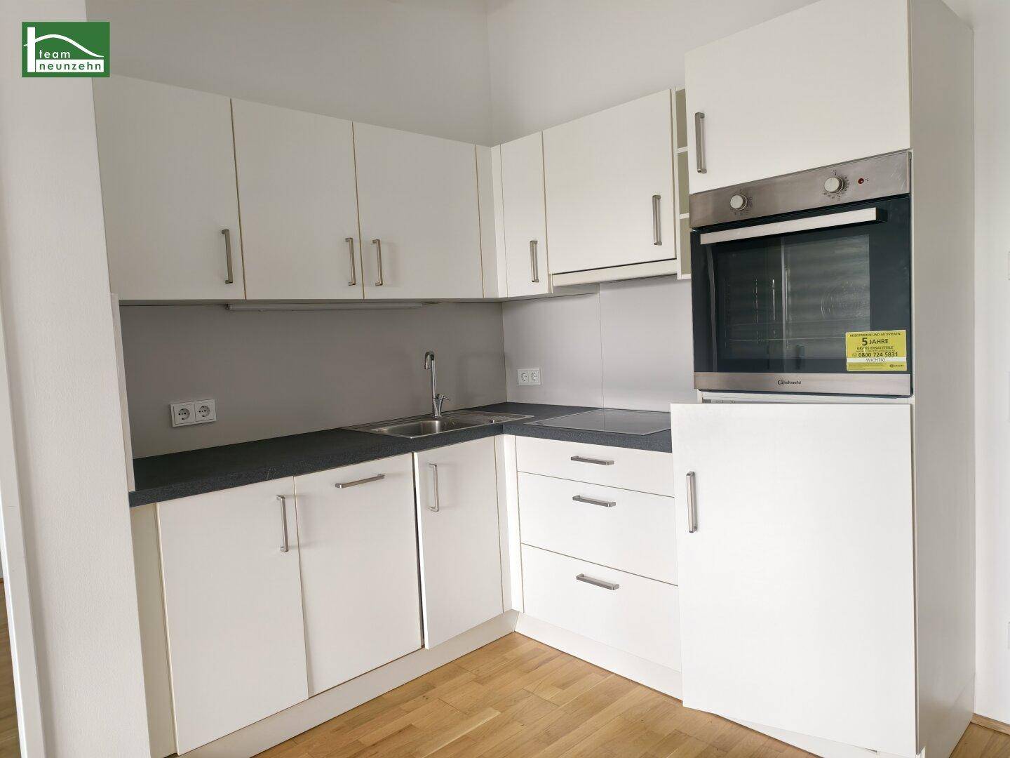 Moderne Küchenzeile mit weißen Schränken, dunkler Arbeitsplatte und integriertem Backofen.