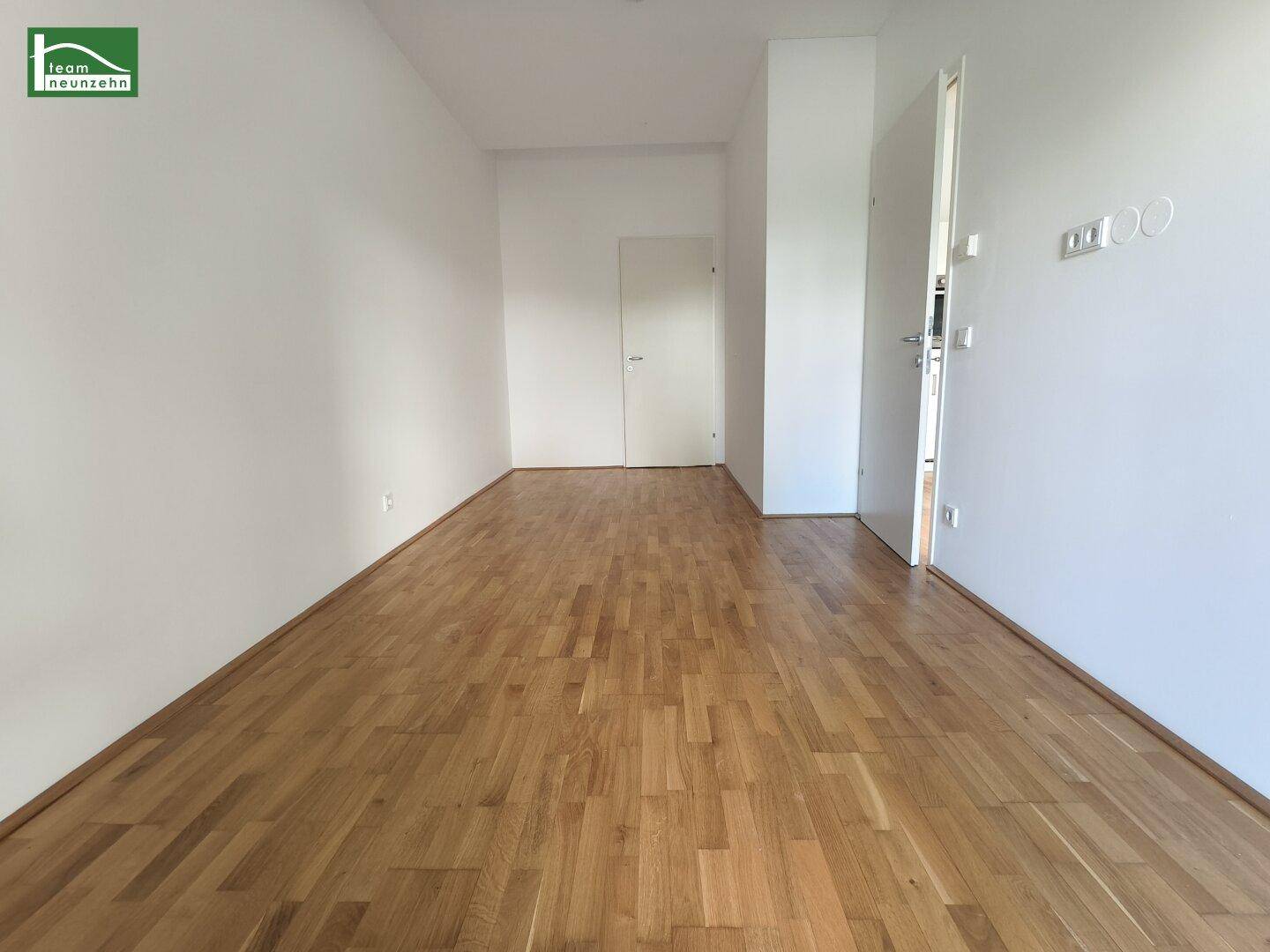 Geräumiger, heller Wohnbereich mit Eichenparkettboden und Eingangstür.